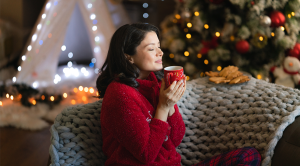Happy woman in red pajamas enjoys the scent of coffee during Christmas morning at home